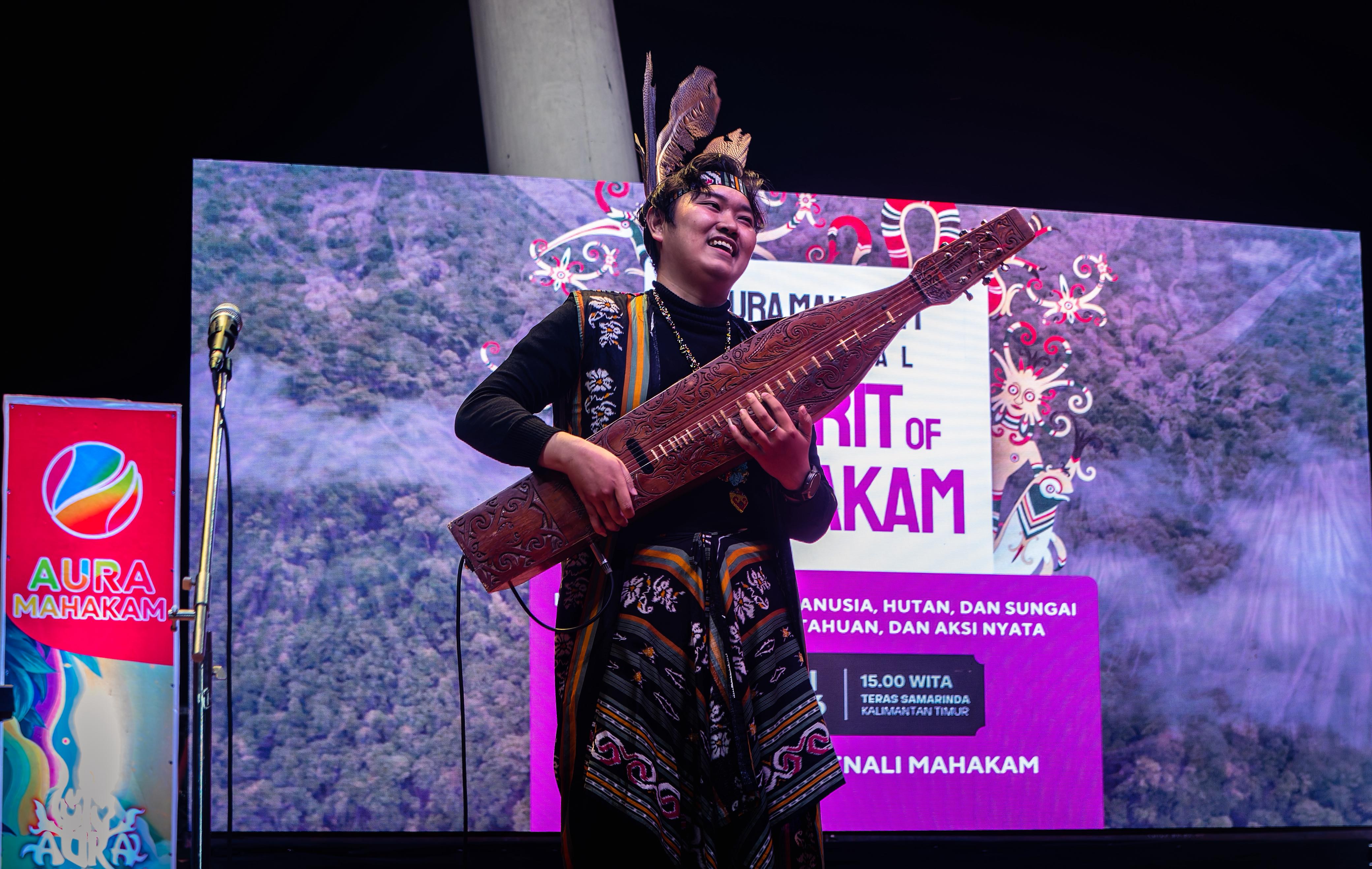 Seorang pemuda memainkan alat musik tradisional Sape di depan layar bertajuk "Spirit of Mahakam".